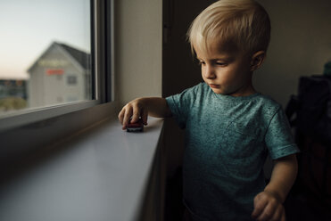 Kleiner Junge spielt mit Spielzeugauto auf der Fensterbank zu Hause - CAVF59967