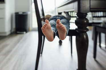 Niedriger Ausschnitt eines kleinen Jungen, der zu Hause auf einem Stuhl am Tisch liegt - CAVF59968