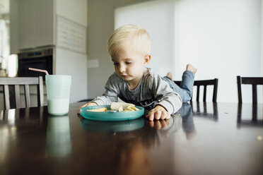 Baby boy eating food while lying on table at home - CAVF59969