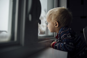 Seitenansicht eines kleinen Jungen, der durch das Fenster schaut, während er zu Hause steht - CAVF59970