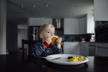 Porträt eines kleinen Jungen, der zu Hause am Esstisch sitzt und isst - CAVF59976