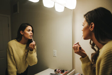 Woman applying lip gloss reflecting on mirror at home - CAVF59988