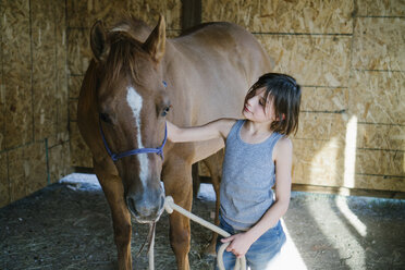 Girl petting horse while standing at barn - CAVF60004
