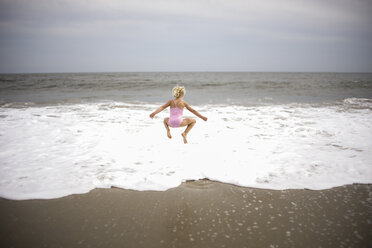 Rear view of playful girl jumping on shore at beach against sky - CAVF60006