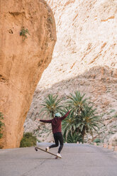 Rear view of woman skateboarding on road by mountains - CAVF60017