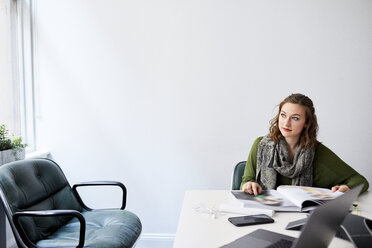 Businesswoman with book looking away while sitting at conference table in office - CAVF60032