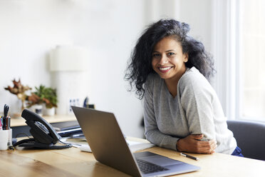 Porträt einer lächelnden Geschäftsfrau mit Laptop am Schreibtisch im Büro - CAVF60073