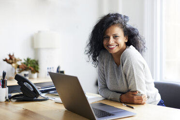 Portrait of smiling businesswoman with laptop computer at desk in office - CAVF60073