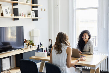 Smiling businesswoman talking with female colleague at desk in office - CAVF60074