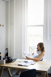 Businesswoman examining documents while sitting at desk in office - CAVF60077