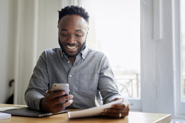 Smiling businessman using mobile phone while sitting at desk in office - CAVF60082