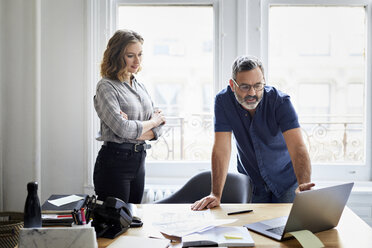 Businessman explaining over laptop computer to female colleague in creative office - CAVF60097