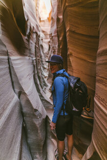 Portrait of female hiker with backpack standing amidst narrow canyons - CAVF60144
