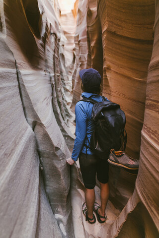 Rückansicht einer Wanderin mit Rucksack, die inmitten enger Schluchten steht, lizenzfreies Stockfoto