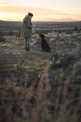 Frau in voller Länge mit Hund auf einem Feld gegen den Himmel bei Sonnenuntergang stehend - CAVF60177