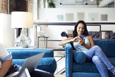 Smiling businesswoman using mobile phone while sitting on sofa at creative office - CAVF60209