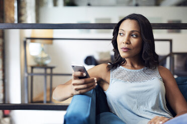 Thoughtful businesswoman with smart phone looking away while sitting on sofa at creative office - CAVF60211