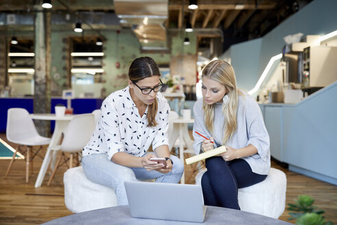 Geschäftsfrauen, die über Smartphone und Laptop diskutieren, während sie im Kreativbüro planen - CAVF60217