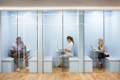 Multi-ethnic business people using laptops while sitting in cubicles at office - CAVF60229