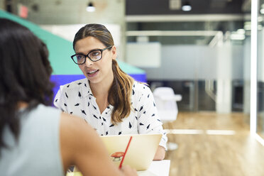 Confident businesswoman discussing with colleague at table in office cafeteria - CAVF60232