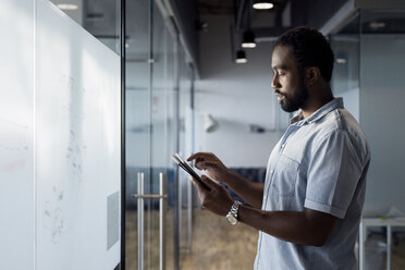 Seitenansicht eines Geschäftsmannes, der ein digitales Tablet benutzt, während er im Bürokorridor steht - CAVF60242
