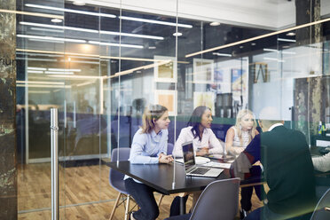 Business people at conference table during meeting seen through glass doors in office - CAVF60251