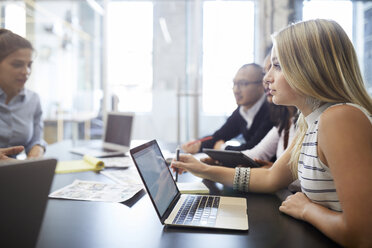 Businesswoman using laptop while sitting with colleagues during meeting at conference table - CAVF60253