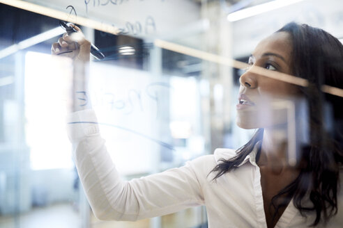 Close-up of businesswoman writing with felt tip pen on glass in board room at office - CAVF60263