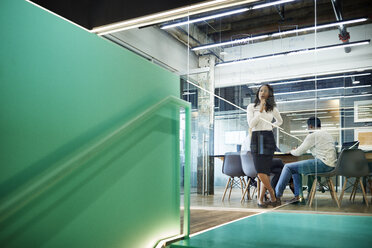 Low angle view of business people in board room seen through glass at office - CAVF60264