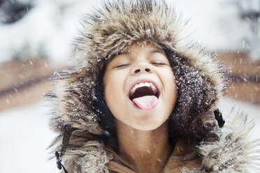 Playful girl with mouth open tasting snow during snowfall - CAVF60286