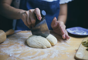 Midsection of woman cutting bread dough at kitchen counter - CAVF60290