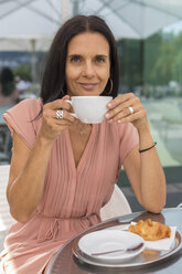 Porträt einer lächelnden reifen Frau, die in einem Straßencafé Kaffee trinkt - JUNF01582