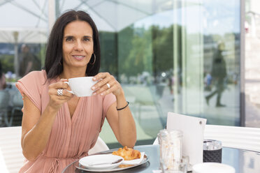 Porträt einer lächelnden reifen Frau, die in einem Straßencafé Kaffee trinkt - JUNF01583