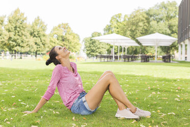 Reife Frau sitzt im Sommer auf einer Wiese und schaut in den Himmel - JUNF01589