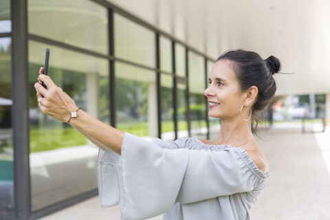 Lächelnde reife Frau nimmt Selfie mit Smartphone im Freien, lizenzfreies Stockfoto