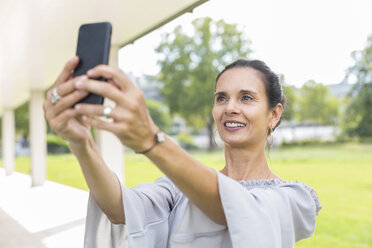 Portrait of smiling mature woman taking selfie with smartphone outdoors - JUNF01598