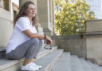 Zufriedene reife Frau sitzt auf einer Treppe im Sommer und ruht sich aus - JUNF01600