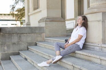 Mature woman sitting on stairs in summer having a rest - JUNF01603