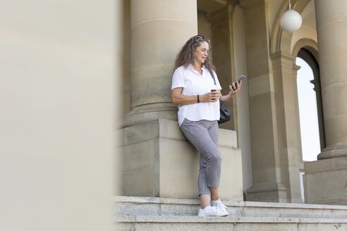 Ältere Frau mit Kaffee zum Mitnehmen schaut auf ihr Handy im Freien - JUNF01606