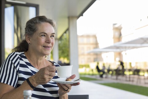 Porträt einer lächelnden reifen Frau, die auf einer Terrasse eine Tasse Kaffee trinkt, lizenzfreies Stockfoto