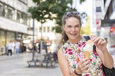 Portrait of smiling mature woman with ice cream cone in the city - JUNF01635