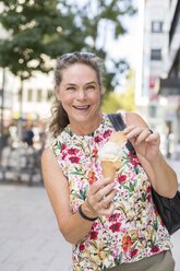 Portrait of smiling mature woman with ice cream cone in the city - JUNF01636