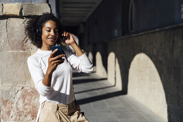 Young casual businesswoman with smartphone and earphones in the city - BOYF01255