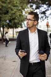 Businessman with takeaway coffee and cell phone in the city on the go - MAUF01935