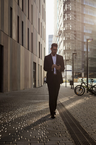 Geschäftsmann, der in der Stadt spazieren geht und sein Mobiltelefon überprüft, lizenzfreies Stockfoto