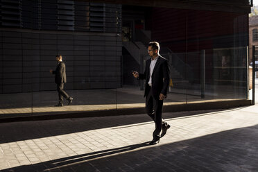 Businessman walking in the city checking cell phone - MAUF01953