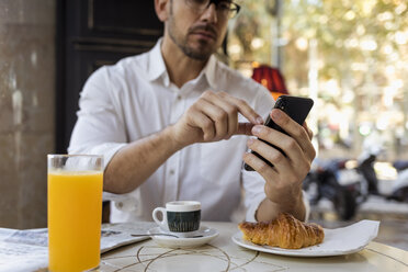 Geschäftsmann frühstückt in einem Café und benutzt ein Mobiltelefon - MAUF01956