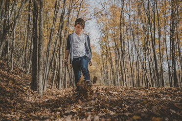 Junge in voller Länge, der im Herbst auf einem Feld gegen Blätter tritt - CAVF60343