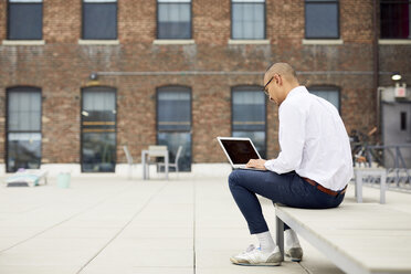 Geschäftsmann in voller Länge, der einen Laptop benutzt, während er auf einem Liegestuhl auf der Terrasse eines Gebäudes sitzt - CAVF60386