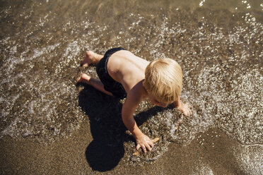 Hoher Winkel Blick auf hemdsärmeligen Jungen spielen am Ufer am Strand während des sonnigen Tages - CAVF60423